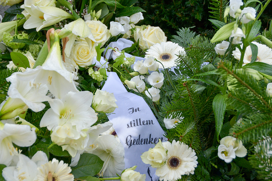 Trauergesteck mit weißen Lilien, Rosen und einer persönlichen Gedenkschleife